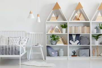 Real photo of white wooden racks with green plants, books and cushions in white teenager room...