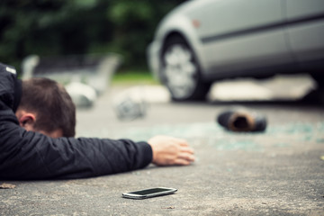 Dead pedestrian lying on the street next to his phone. Shoe, broken glass and car blurred in the...