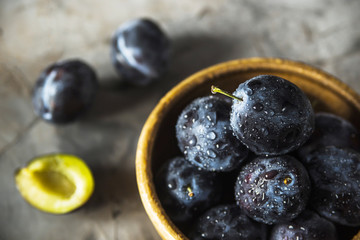 Ripe blue plums in a clay bowl on a gray table. Summer seasonal fruit concept