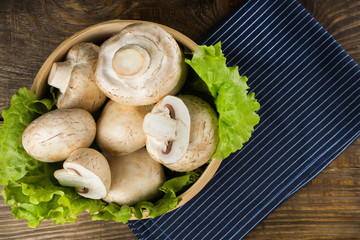 Round container with lettuce leaves and mushrooms on wooden table. Top view.