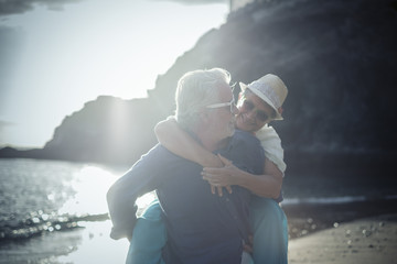 happy senior couple have fun and enjoy outdoor leisure activity at the beach. the man carry the...