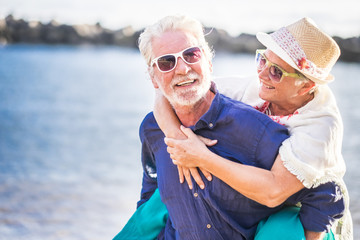 happy senior couple have fun and enjoy outdoor leisure activity at the beach. the man carry the...