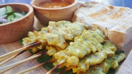 Pork Satay and bread with peanut sauce and pickles which are cucumber slices and onions on wood plate and bowl. 