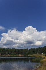 textured white clouds against the backdrop of a forest lake and tall forest trees