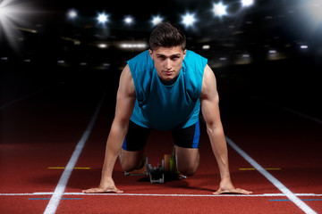 Sprinter leaving starting blocks on the running track in front of big modern stadium with lights....