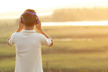 teenager in headphones listening to music at sunset in the field