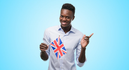 Young african american man holding United Kingdom flag very happy pointing with hand and finger to...