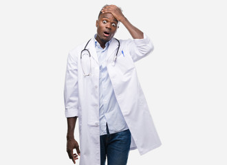 Young african american man wearing doctor coat stressed with hand on head, shocked with shame and...