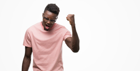 Young african american man wearing pink t-shirt angry and mad raising fist frustrated and furious...