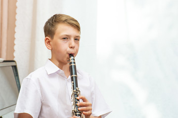 The boy plays the clarinet near the black piano by the window. Musicology, music education and...