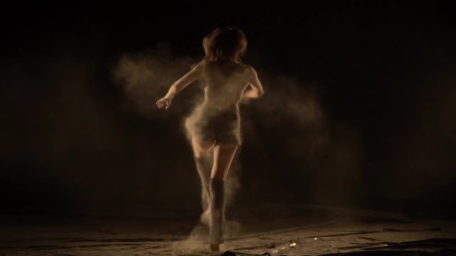 Ballerina in sportswear is spinning in the dance with her falling sand, slow motion