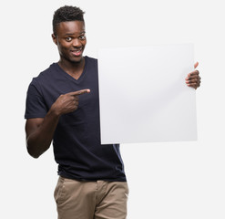 Young african american man holding a banner very happy pointing with hand and finger