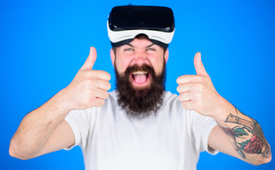 Man with beard and mustache with VR glasses, blue background. Guy with VR glasses or head mounted display. Hipster on happy face shows thumbs up gesture, defocused. VR technology concept