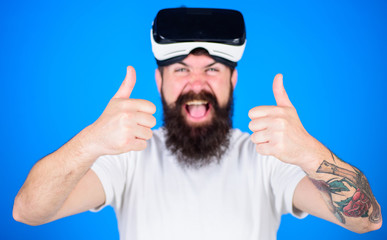 Naklejka premium Man with beard and mustache with VR glasses, blue background. Guy with VR glasses or head mounted display. Hipster on happy face shows thumbs up gesture, defocused. VR technology concept