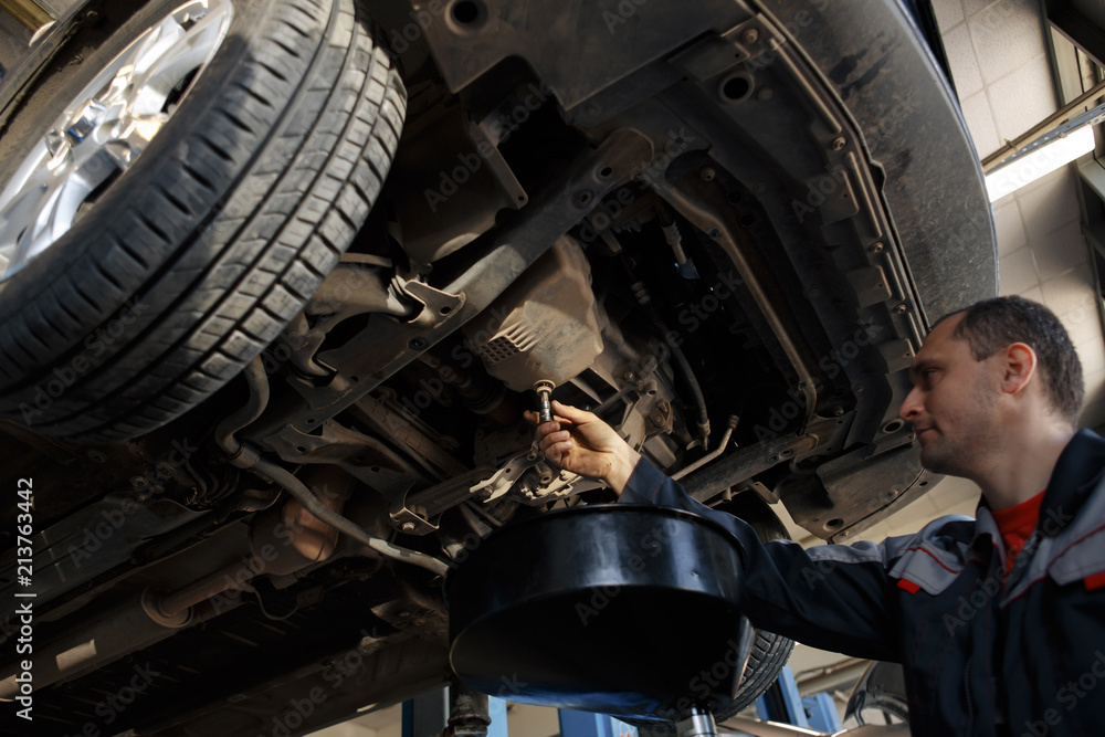 Poster profecional car mechanic changing motor oil in automobile engine at maintenance repair service stati