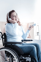 Dreamy mood. Pretty invalid woman keeping smile on her face while touching headphones