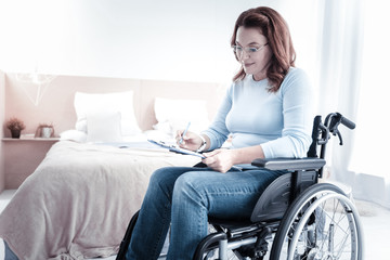 Making notes. Delighted young woman sitting on her wheelchair while reading documents
