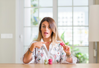 Young woman at home eating macarons very happy pointing with hand and finger