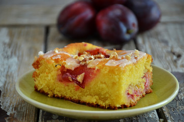 A piece of cake with plums on a green saucer on a wooden background