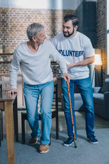 Heart of gold. Attractive content bearded man smiling and helping an old man while he walking with his stick