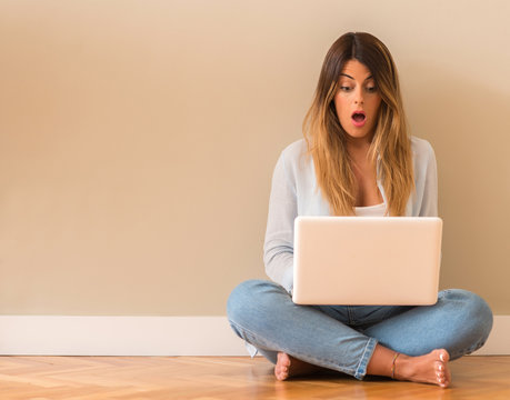 Young Beautiful Woman Suprised Sitting On The Floor With Computer Looking At The Laptop.