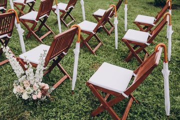 In area of wedding ceremony on the green grass in the park are chairs for guests