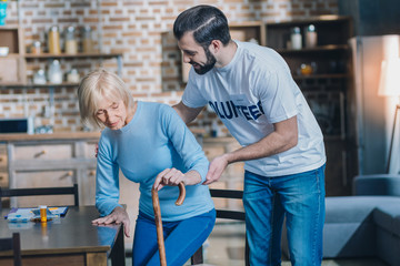Relying on you. Joyful young man smiling and helping an old woman while she standing up