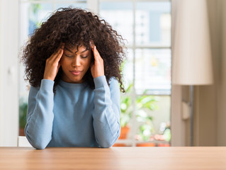 African american woman at home with hand on head for pain in head because stress. Suffering...