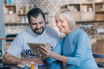 My grandchildren. Alert old woman smiling and showing her family photos to a young man