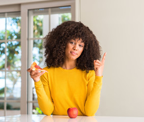 African american woman choosing between apple and pizza slice very happy pointing with hand and finger to the side