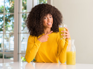African american woman drinking healthy fruit juice at home very happy pointing with hand and finger