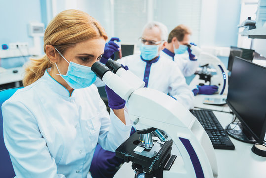 Scientific worker. Serious lab assistant sitting in semi position while working with microscope