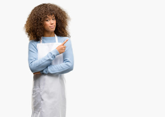 African american shop owner woman wearing an apron pointing away side with finger