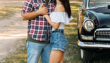 embrace.Love and affection between a young couple at the park, near the old car. a guy in a plaid plane and jeans, a girl in shorts and a white jacket. They get together in the forest for a walk.