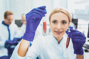 Detail examination. Cheerful lab assistant keeping smile on her face while looking at test tubes...