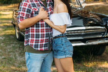 embrace.Love and affection between a young couple at the park, near the old car. a guy in a plaid plane and jeans, a girl in shorts and a white jacket. They get together in the forest for a walk.