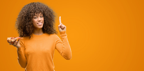 African american woman with a pizza slice surprised with an idea or question pointing finger with...