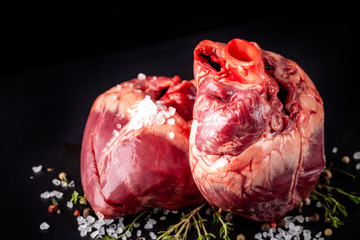 Beef raw heart on a black background with rosemary and spices.