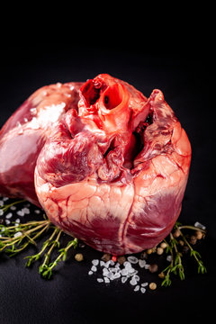 Beef raw heart on a black background with rosemary and spices.