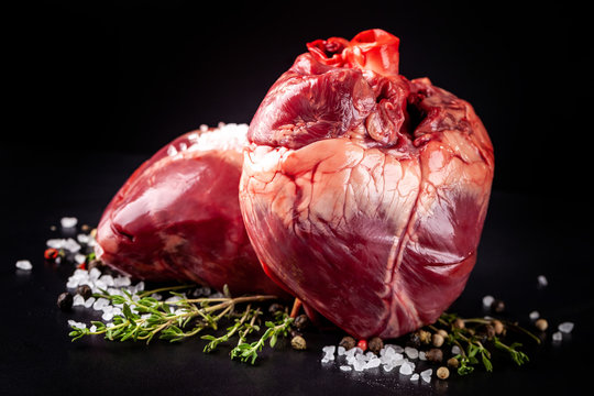 Beef raw heart on a black background with rosemary and spices.