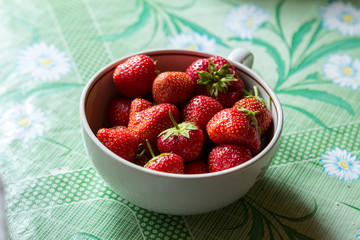 ripe strawberry berry with green leafs in a plate on a green background