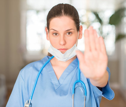 Young nurse woman wearing mask and stethoscope with open hand doing stop sign with serious and confident expression, defense gesture
