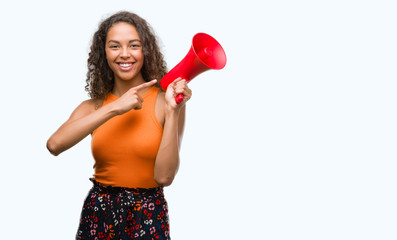 Young hispanic woman holding megaphone very happy pointing with hand and finger