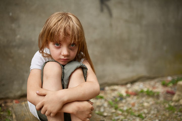 Street photo of girl orphan with holen knees in dirty alley.