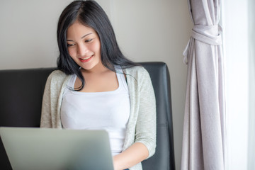 Beautiful attractive young Asian woman using laptop at living room in the morning 