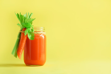 Organic carrot juice with carrots, celery on yellow background. Vegetable smothie in glass jar. Copy space. Summer food concept. Healthy detox eating, alkaline diet