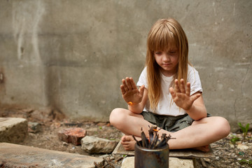 Neglected lonely child warming her hands in the fire from the can under the street wall in the...
