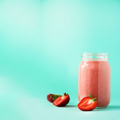 Glass with vegan strawberry smoothie on blue background with copy space. Square crop. Summer food and clean eating concept, vegan diet. Pink detox beverage with fresh berries