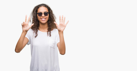 Young hispanic woman wearing sunglasses showing and pointing up with fingers number eight while...