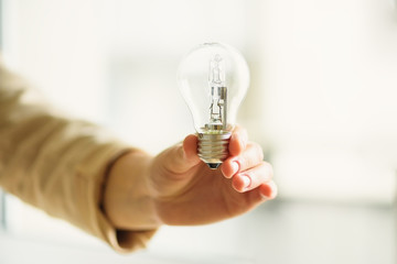 Woman hand holding light bulb on cream background with copy space. Creative idea, new business plan, motivation, innovation, inspiration concept.
